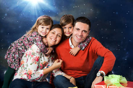 Close up portrait of happy young couple with their two kids next to christmas gift.の写真素材