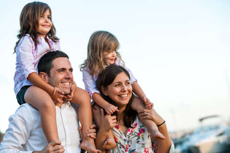 Close up portrait of young couple with kids on shoulders at sunset.の写真素材