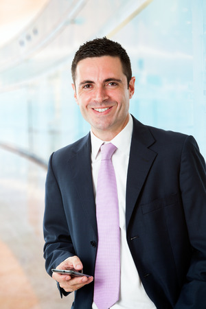 Portrait of Handsome young businessman standing with smart phone at work.の写真素材