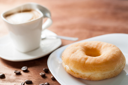 Macro close up of Doughnut on wooden table with cup of creamy coffee in background.の写真素材
