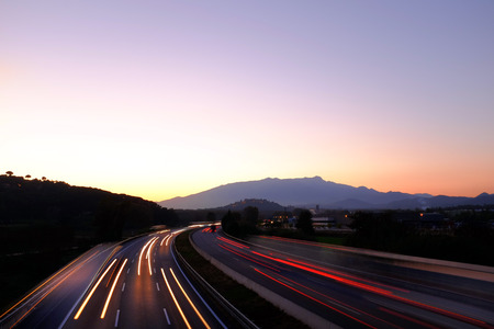 Colorful scene of moving vehicles on busy highway at dawn leaving beams of red lights.の写真素材