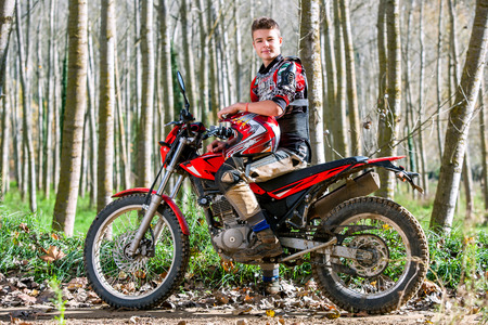 Portrait of attractive teen boy sitting on motocross motorbike in woods.の写真素材