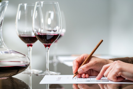 Extreme close up of female hand taking notes at red wine tasting.の写真素材