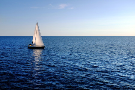 Yacht with reflection sailing on open sea.