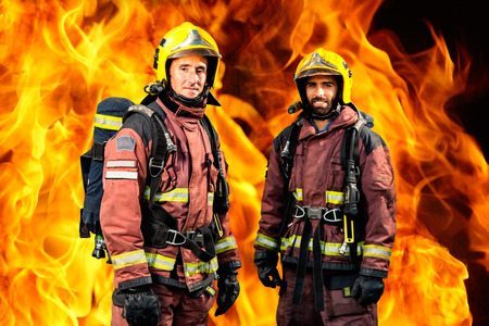 Conceptual portrait of two firemen standing against burning fire background.の写真素材