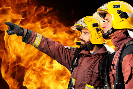 Fireman showing companion possible fire against Orange and yellow flames in background.の写真素材