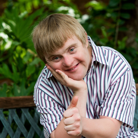 Close up portrait of cute boy with down syndrome doing thumbs up in garden.の写真素材