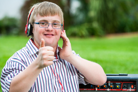 Close up portrait of down syndrome boy with headset doing thumbs up outdoors.の写真素材