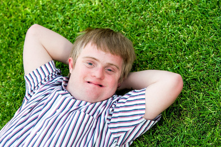 Close up portrait of handicapped boy laying with hands under head on green grass.の写真素材