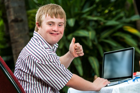 Portrait of handicapped student doing thumbs up sign next to laptop outdoors.の写真素材