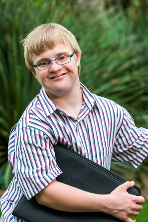 Close up portrait of young student with down syndrome holding files outdoors.の写真素材