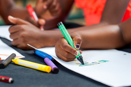 Macro close up of African kids hands drawing with wax crayons at desk.の写真素材