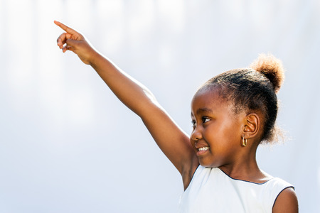 Portrait of little African girl pointing with finger and looking at corner.Isolated against light background.の写真素材
