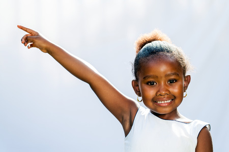 Portrait of little African girl pointing at corner with finger.Isolated against light background.の写真素材