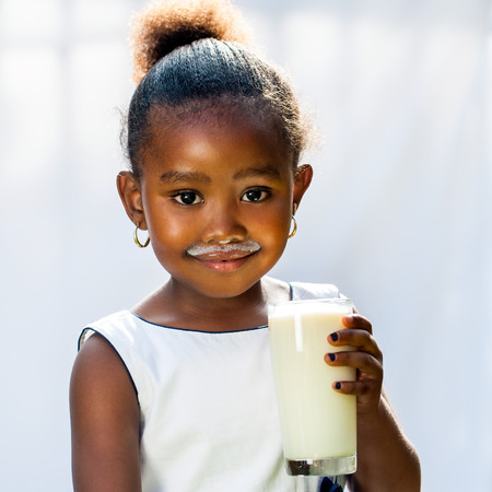 Close up portrait of adorable little African girl drinking glass of milk.Isolated against light background.の写真素材