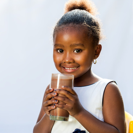 Close up portrait of adorable African girl drinking milk chocolate drink.Isolated on light background.の写真素材
