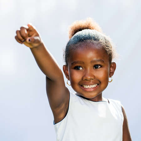 Portrait of small African girl pointing with finger into distance.Isolated against light background.の写真素材