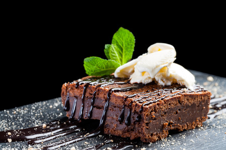 Macro close up of appetizing chocolate brownie with dark chocolate dressing and vanilla ice cream against black background.