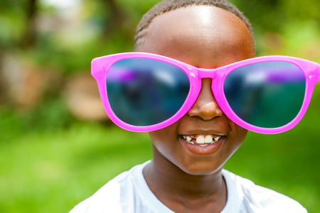 Close up face shot portrait of cute African boy wearing huge over sized sun glasses outdoors.の写真素材