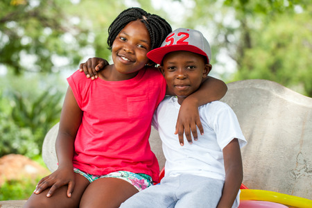 Close up portrait of two African kids sitting together on bench in park.の写真素材