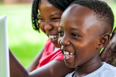 Close up face shot of African kids laughing at movie scene on digital tablet outdoors.の写真素材