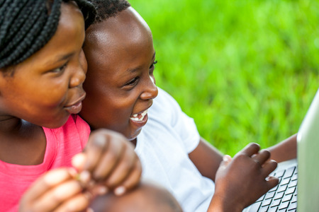 Close up face shot of African kids laughing at scene on laptop outdoors.の写真素材