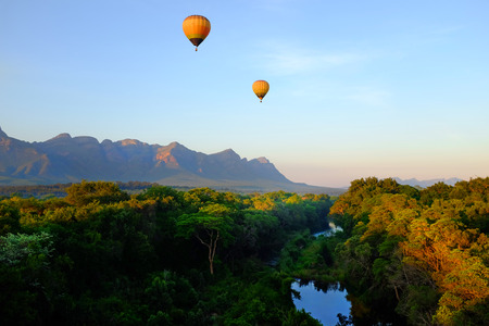 Two hot air balloons riding over african landscape with mountains in background at sunrise.の写真素材