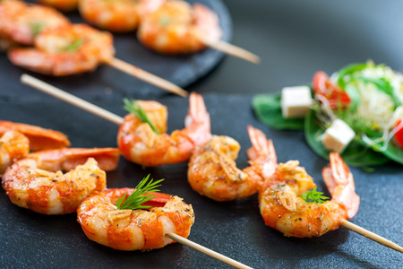 Macro close up of catering shrimp brochettes grilled with herbs. Out of focus salad in background.の写真素材