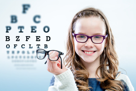 Close up portrait of young girl holding glasses with test chart in background.の写真素材