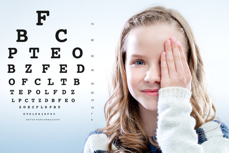 Close up portrait of Girl reviewing eye sight closing eye with hand.Test chart in background.の写真素材