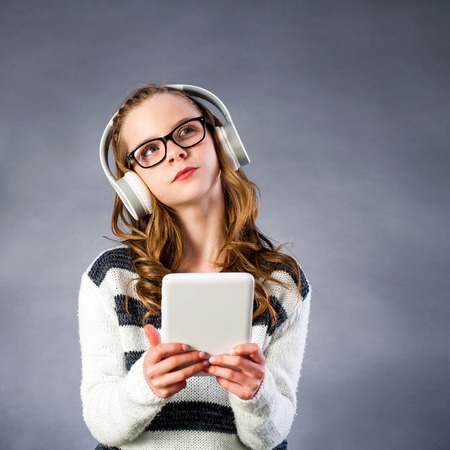 Close up portrait of Cute girl with head phones and digital tablet looking at corner. Girl wearing glasses with thinking face expression against dark background.の写真素材