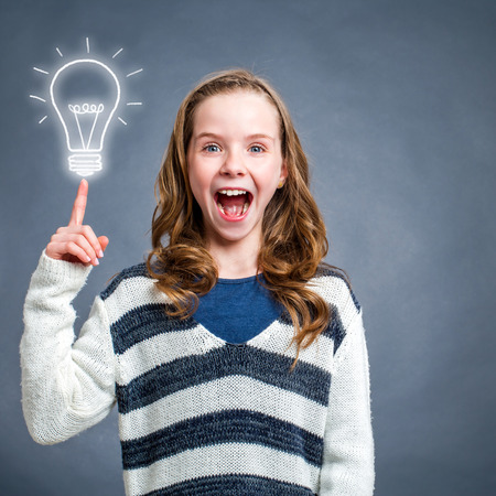 Conceptual portrait of cute surprised girl with shocking face expression pointing at light bulb against dark background.の写真素材