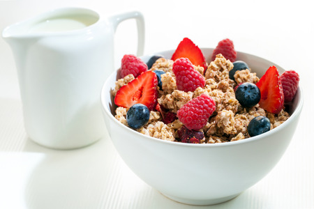 Macro close up of crunchy muesli with red fruit.White bowl with muesli and milk jug in background.の写真素材