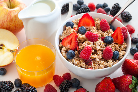 Macro close up of appetizing crunchy muesli bowl with red fruit. Fruits and fresh orange juice next to bowl.の写真素材