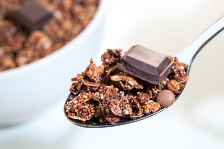 Macro close up of spoon with crunchy chocolate muesli and out of focus bowl in background.の写真素材