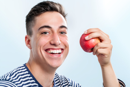 Extreme close up of Handsome young teen holding red apple and  showing healthy teeth.の写真素材