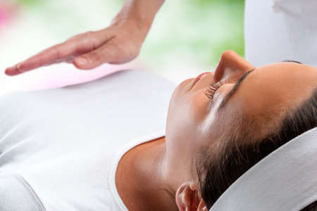 Close up portrait of young woman relaxing at reiki session with therapist hand in background.