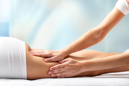 Therapist massaging upper back part of female leg. Hands applying pressure on hamstrings.の写真素材