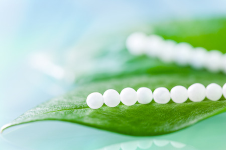 Extreme close up of Multiple homeopathic pills on green leaves against blue background.の写真素材