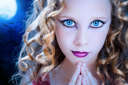 Extreme close up facial portrait of young Girl with big blue eyes. Beauty cosmetic make up on pre teen with graveyard at full moon in background.の写真素材