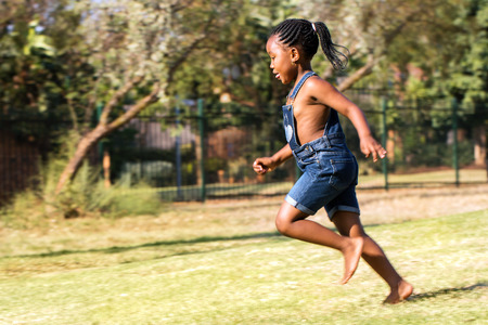 Close up action portrait of african kid running in park. Side view of little ponytailed girl in motion.の写真素材