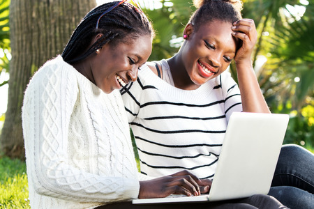 Close up outdoor portrait of two afro american teen girls socializing on laptop in park.の写真素材