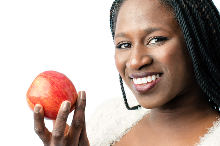 Macro close up of attractive african girl with toothy smile holding red apple. Isolated on white background.の写真素材