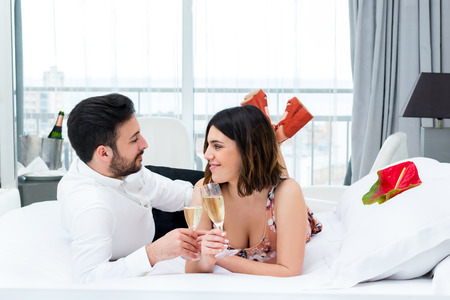 Close up portrait of young couple on honeymoon in hotel.Man and woman drinking champagne on bed in suite.の写真素材