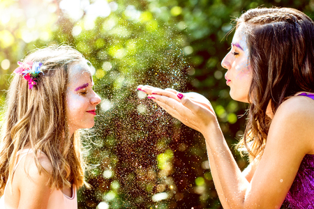 Portrait of girl blowing gold glitter towards younger kid in forest.