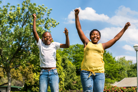 Close up action portrait of two  african kids jumping together in outdoor park.の写真素材