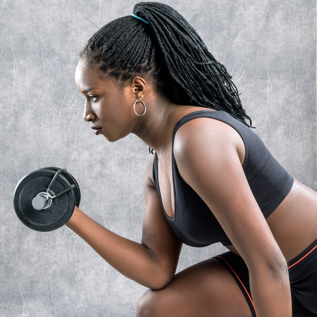 Close up portrait of african teen girl working out with dumbbell.Side view of young woman in sportswear against grey background.の写真素材