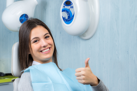 Close up portrait of cute young woman doing thumbs up at appointment in dental clinic.の写真素材