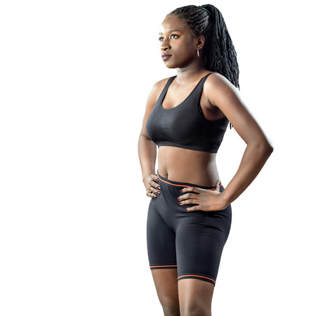 Medium shot of attractive african teen girl in sportswear standing with hands on hips. Young woman looking aside isolated on white background.の写真素材
