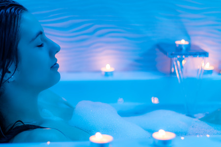 Close up  Low light ambient portrait of woman enjoying foam bath.Blue ambient with decorative candles along bath tub.の写真素材